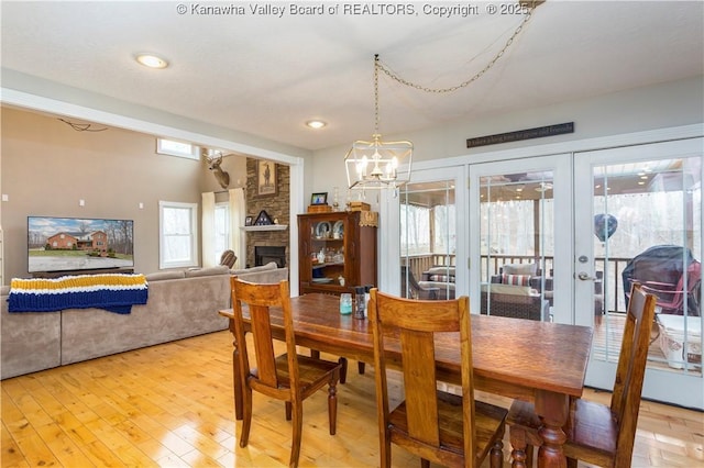 dining area featuring french doors, a fireplace, light wood-type flooring, an inviting chandelier, and recessed lighting