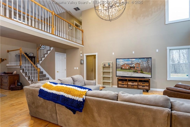 living room featuring a high ceiling, an inviting chandelier, wood finished floors, visible vents, and stairway