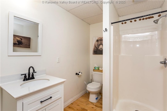 full bath with vanity, wood finished floors, toilet, a drop ceiling, and a stall shower