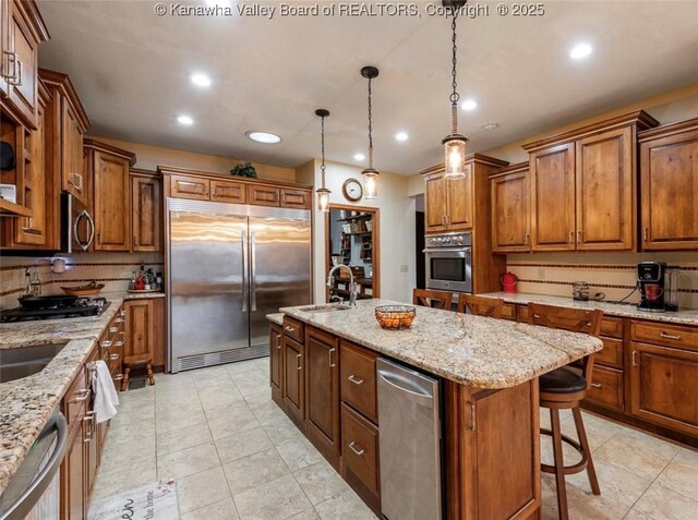 356 Latigo Pt, Milton, WV 25541 - kitchen featuring stainless steel appliances, an island with sink, brown cabinets, backsplash, and a breakfast bar
