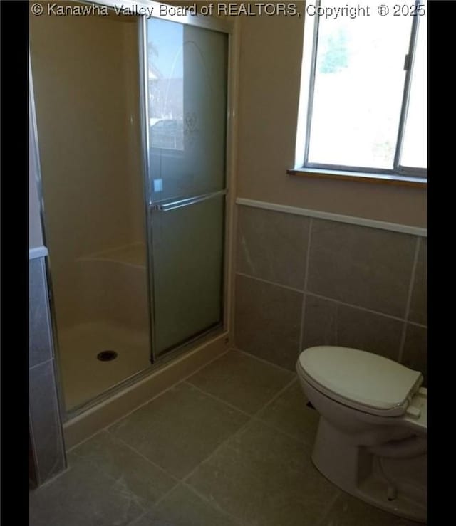 full bath with a stall shower, tile patterned floors, toilet, and tile walls
