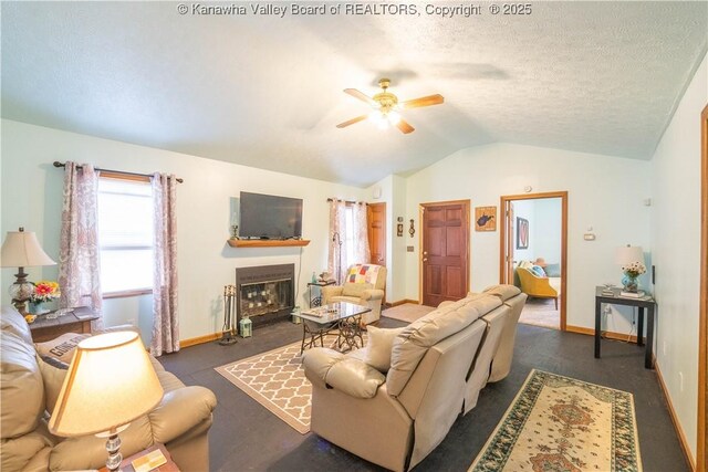 living area featuring a fireplace with flush hearth, a textured ceiling, baseboards, a ceiling fan, and lofted ceiling