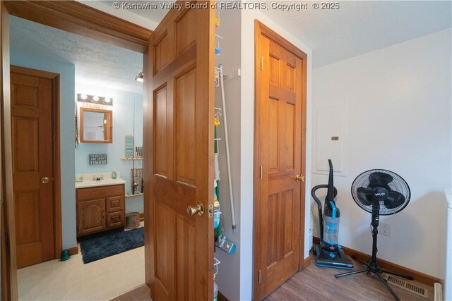 corridor featuring a textured ceiling, visible vents, baseboards, wood finished floors, and a sink