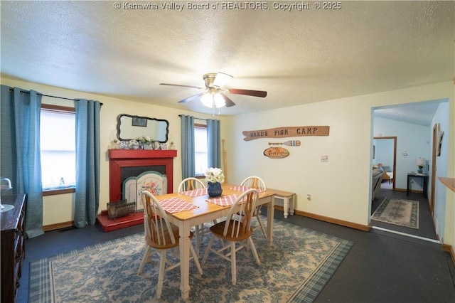 dining area featuring a textured ceiling, a fireplace with raised hearth, baseboards, and a ceiling fan