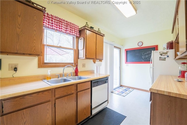kitchen with light countertops, a sink, brown cabinetry, and white appliances