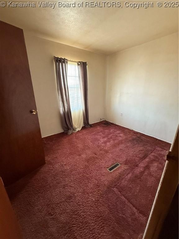 empty room featuring carpet flooring, a textured ceiling, and visible vents
