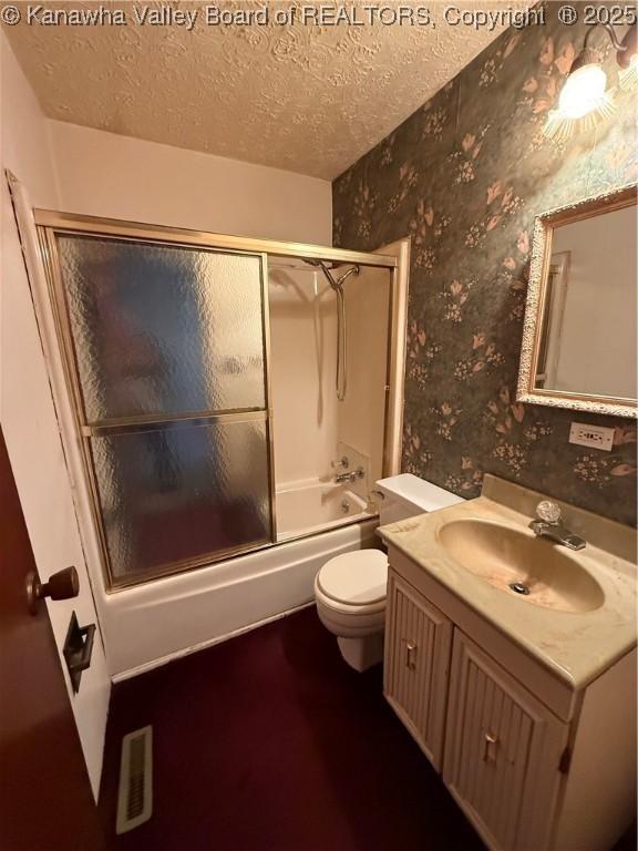 bathroom with a textured ceiling, bath / shower combo with glass door, wallpapered walls, toilet, and vanity