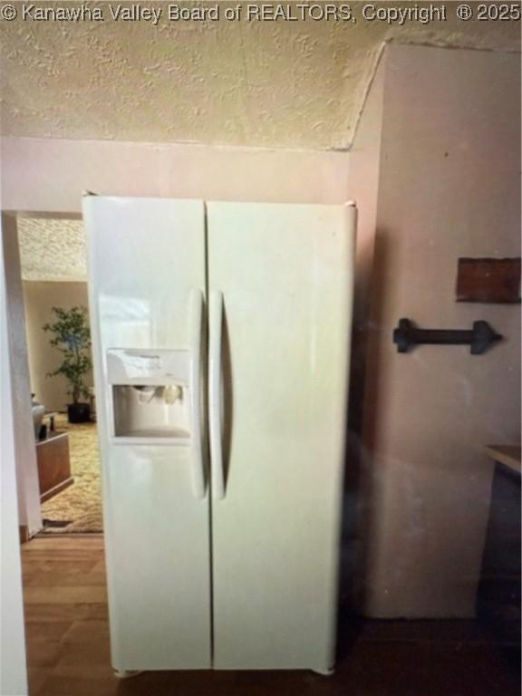 interior details with a textured ceiling, wood finished floors, and white fridge with ice dispenser
