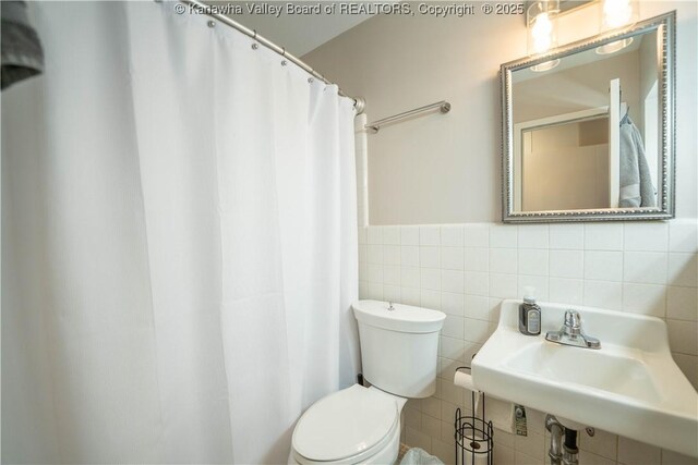 bathroom featuring tile walls, toilet, a shower with shower curtain, a wainscoted wall, and a sink