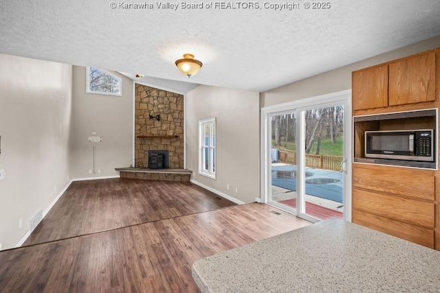 25 Lilly Hls, South Charleston, WV 25309 - unfurnished living room with wood finished floors, a textured ceiling, baseboards, and a stone fireplace