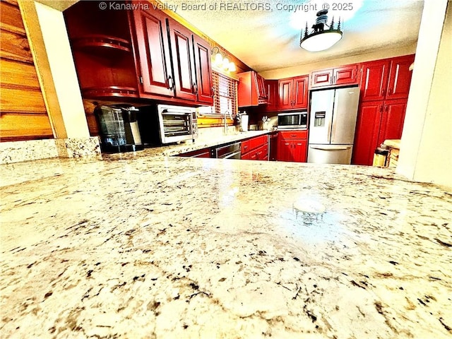kitchen featuring dishwashing machine, white refrigerator with ice dispenser, a textured ceiling, stainless steel microwave, and reddish brown cabinets