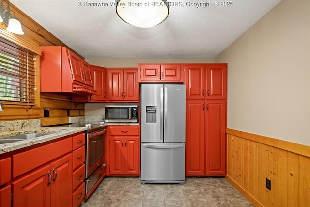 23 Mindia Ln, Alum Creek, WV 25003 - kitchen featuring appliances with stainless steel finishes, wooden walls, a wainscoted wall, light stone countertops, and a sink