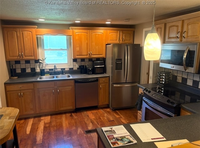 kitchen with appliances with stainless steel finishes, dark countertops, tasteful backsplash, and a sink