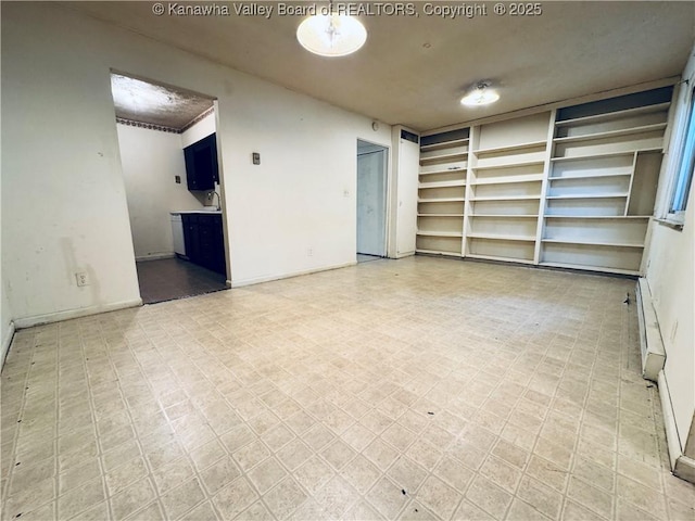 unfurnished room with baseboard heating, baseboards, and light floors