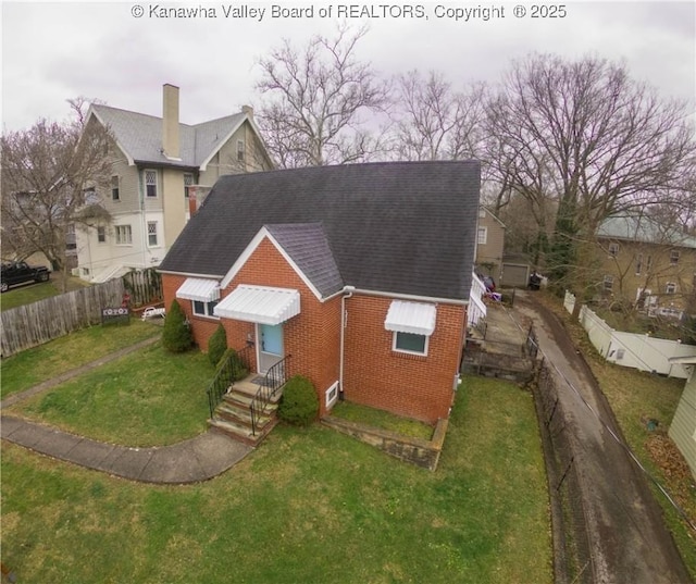 view of front of property with roof with shingles, a fenced backyard, a front lawn, and brick siding