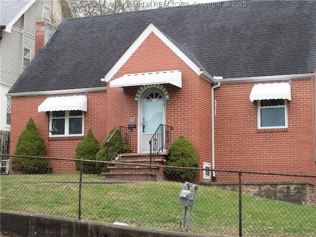 tudor house with a front yard, a shingled roof, brick siding, and a fenced front yard