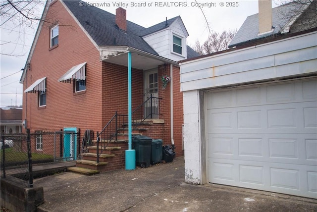 exterior space with a chimney, driveway, brick siding, a garage, and fence