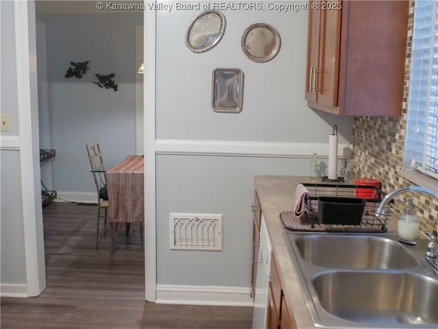 kitchen with dark wood-type flooring, visible vents, a sink, baseboards, and backsplash