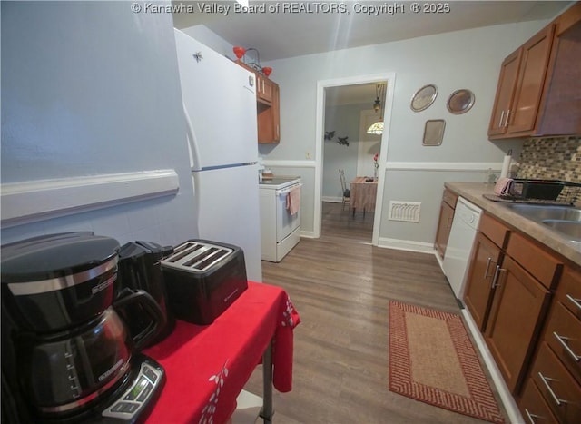 kitchen with tasteful backsplash, brown cabinetry, white appliances, and dark wood-style floors