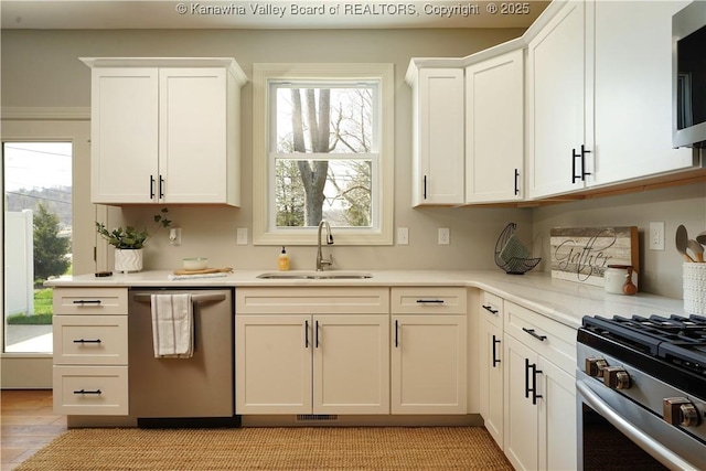 kitchen with stainless steel appliances, light countertops, a sink, and white cabinetry