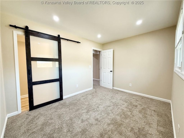unfurnished bedroom featuring carpet floors, baseboards, recessed lighting, and a barn door