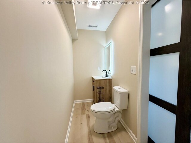 half bathroom with visible vents, baseboards, toilet, vanity, and wood finished floors