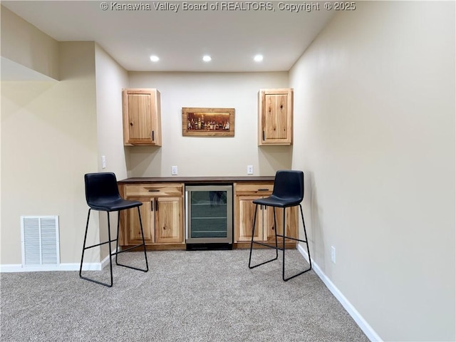 bar with light carpet, visible vents, beverage cooler, and baseboards