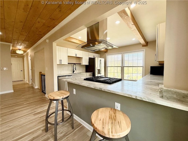 kitchen featuring tasteful backsplash, a peninsula, appliances with stainless steel finishes, a sink, and island range hood