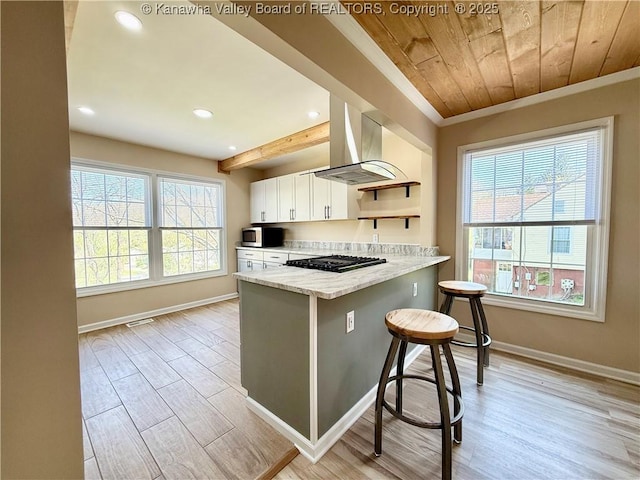 kitchen featuring stainless steel microwave, white cabinetry, open shelves, light wood-style floors, and wall chimney exhaust hood
