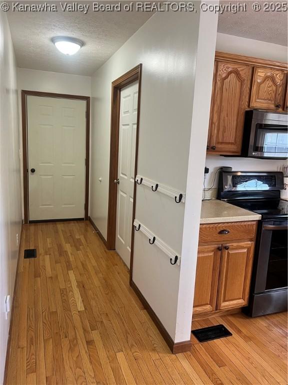 corridor with light wood-style floors, a textured ceiling, and baseboards