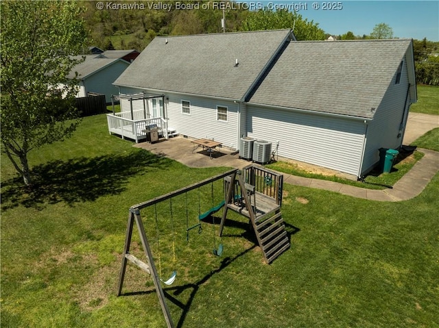 rear view of house featuring a shingled roof, a deck, a playground, a patio, and a yard