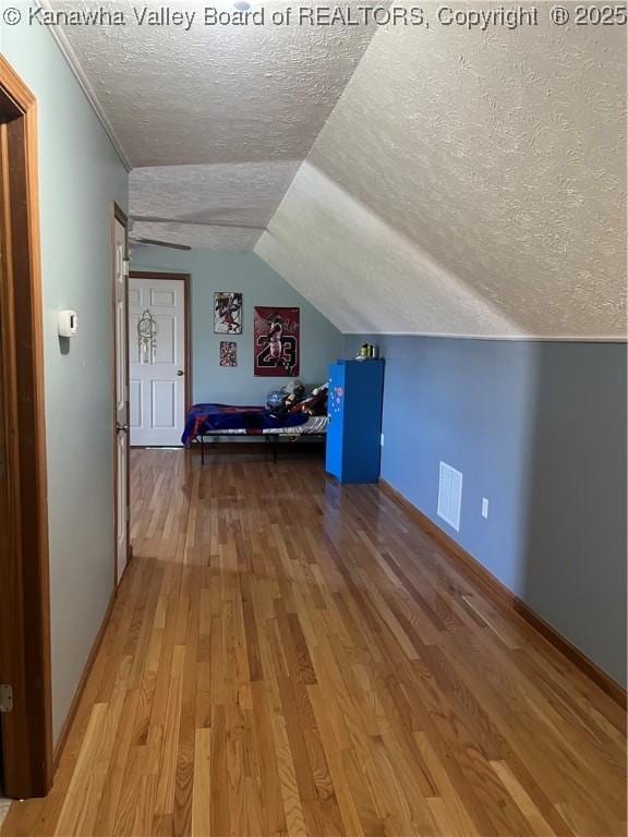 additional living space with a textured ceiling, baseboards, wood finished floors, lofted ceiling, and visible vents