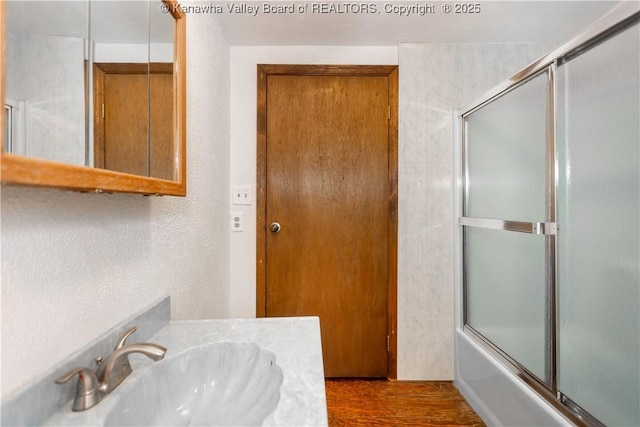 full bath with wood finished floors, shower / bath combination with glass door, a textured wall, and vanity