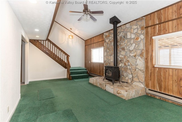 unfurnished living room with plenty of natural light, stairway, carpet floors, a wood stove, and a baseboard radiator