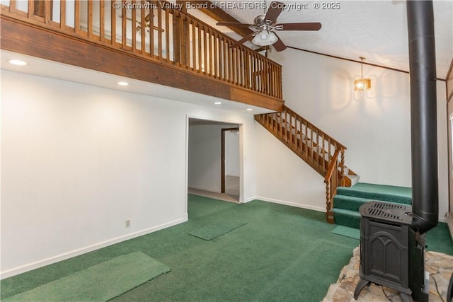 interior space featuring baseboards, a high ceiling, a wood stove, ceiling fan, and carpet flooring