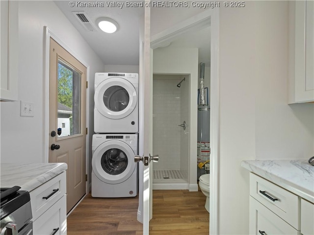 laundry area featuring wood finished floors, visible vents, stacked washer / dryer, and laundry area