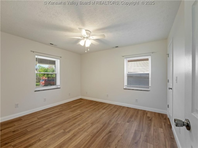 empty room featuring light wood-style flooring, a textured ceiling, ceiling fan, and plenty of natural light