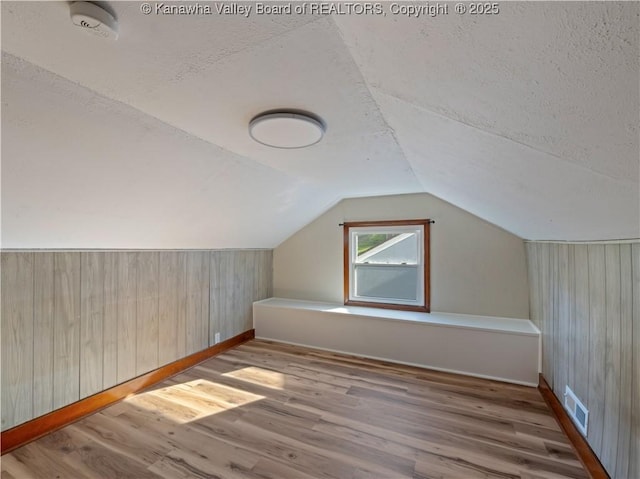 bonus room with wood walls, wood finished floors, visible vents, baseboards, and a textured ceiling