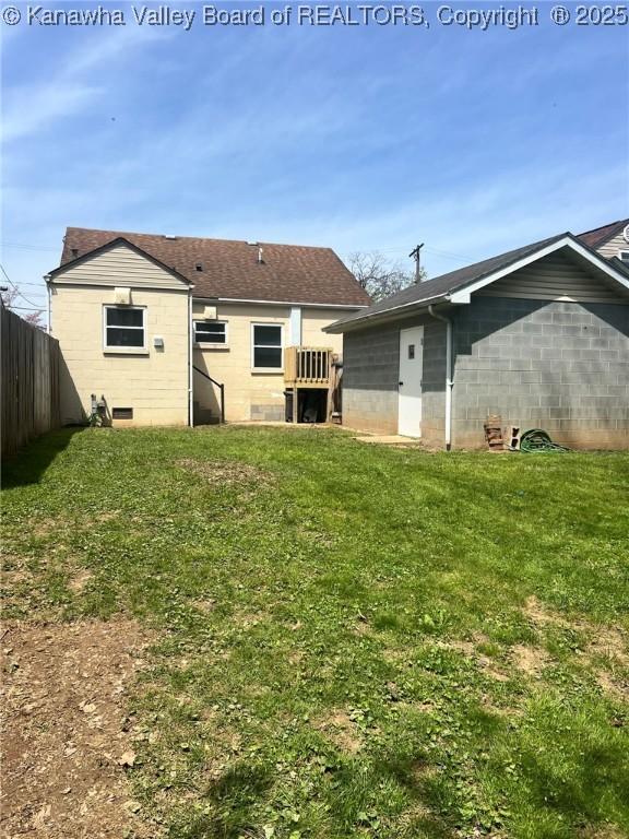 rear view of house with concrete block siding, a lawn, and fence