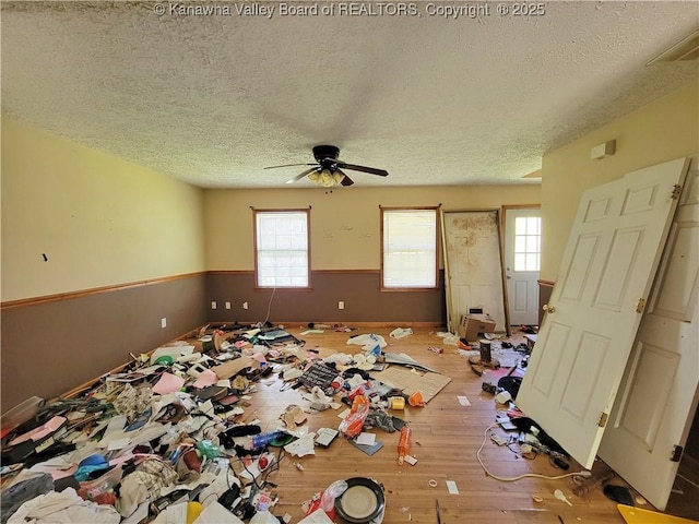 interior space with a ceiling fan, a textured ceiling, wainscoting, wood-type flooring, and visible vents