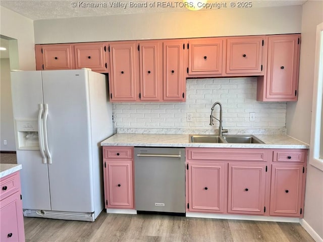 kitchen with stainless steel dishwasher, a sink, white refrigerator with ice dispenser, light wood-style floors, and backsplash