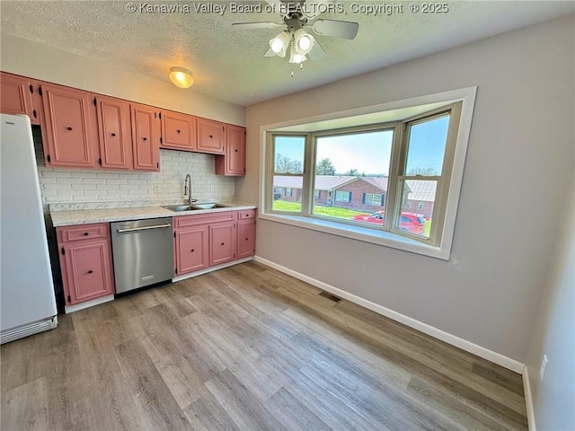 kitchen featuring a ceiling fan, a sink, dishwasher, baseboards, and freestanding refrigerator