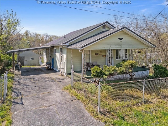 view of front facade featuring aphalt driveway, a carport, covered porch, fence, and metal roof
