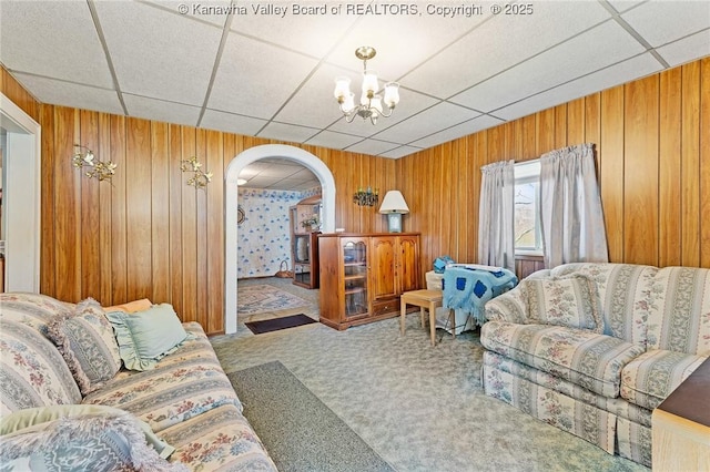 living area with an inviting chandelier, carpet flooring, arched walkways, and a drop ceiling