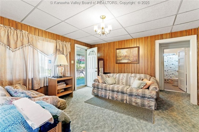carpeted living room featuring wooden walls, a chandelier, and a drop ceiling