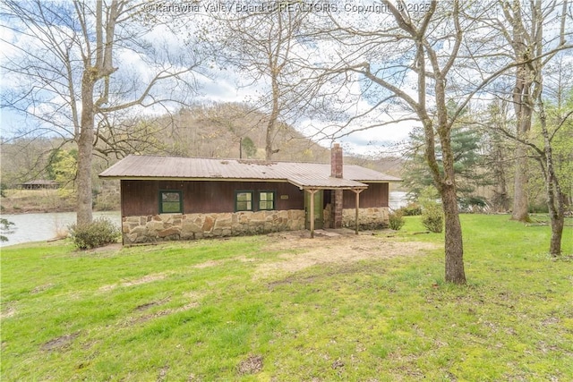 exterior space featuring a lawn, stone siding, and a chimney