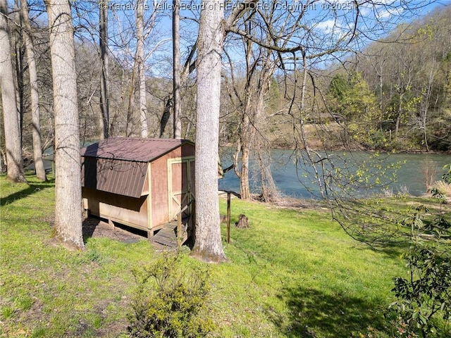 view of yard with a forest view, an outbuilding, a storage shed, and a water view
