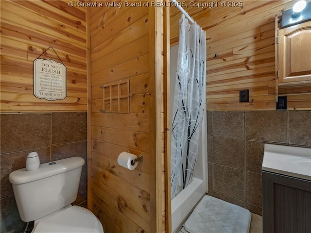 full bathroom with wood walls, toilet, vanity, tile walls, and shower / bath combo with shower curtain
