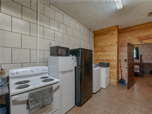 kitchen with wooden walls, visible vents, washing machine and clothes dryer, black appliances, and a textured ceiling