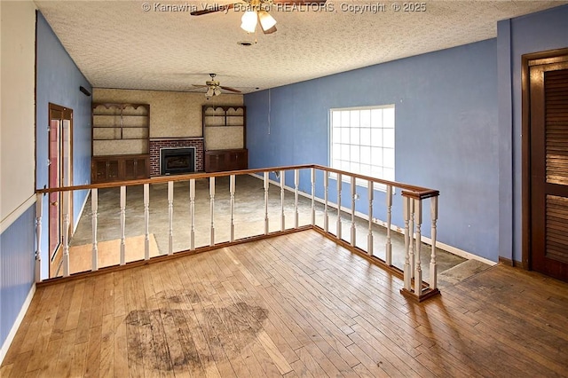 455 Kane St, Milton, WV 25541 - unfurnished room with a brick fireplace, a textured ceiling, ceiling fan, and wood-type flooring